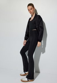 Zwart sportoutfit bestaande uit een cropped top en flared leggings. Het materiaal is soepel en rekbaar; inclusief een comfortabele, met rits afsluitbare jacket.