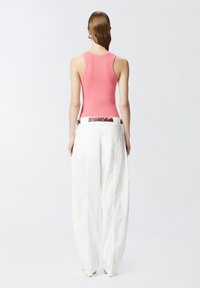 Majica bez rukava ružičaste boje i bijele široke hlače s uzorkovanom remenom. Tkanina djeluje glatko s ležernim krojem i širokim siluetom.
