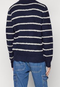 Marinblå randig tröja med fluffiga vita linjer, rund halsringning och ribbade manschetter. Bärs med blå cargobyxor, som visar upp en avslappnad passform och textur.