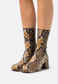 Botki na wysokim obcasie w stylu kostki z wężowym wzorem w odcieniach brązu i czerni, o teksturowanej powierzchni i zwężonym nosku.