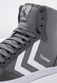 Shoe de cano alto com exterior em tecido cinzento, design em chevrão branco, detalhes em camurça cinzenta e ilhós pretos. Apresenta logo na língua.