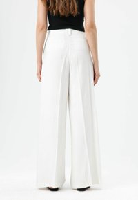 Pantalon blanc à jambes larges avec une texture lisse, présentant une taille haute et une fermeture à bouton à l'arrière, vu de dos.