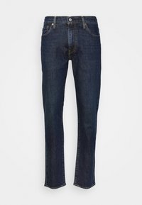 Jean en denim bleu foncé slim avec bouton devant et poches sur un fond clair uni.