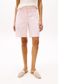 Rosa Baumwollshorts mit geradem Schnitt, ausgestattet mit einem Knopfverschluss und umgeschlagenem Saum, kombiniert mit geflochtenen Slippers.