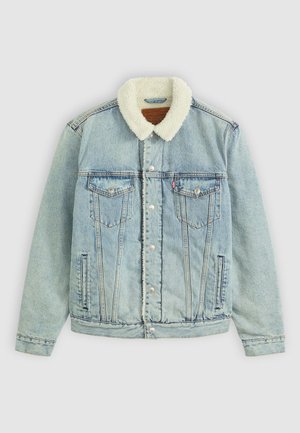 Chaqueta de denim azul claro con un cuello de peluche blanco. Presenta bolsillos en el pecho, botones a presión y un ajuste relajado con detalles de costura visibles.