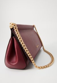 Sac à main en cuir bourgogne avec une bandoulière en chaînettes dorées et un logo de marque discret sur le rabat avant, sur fond blanc.