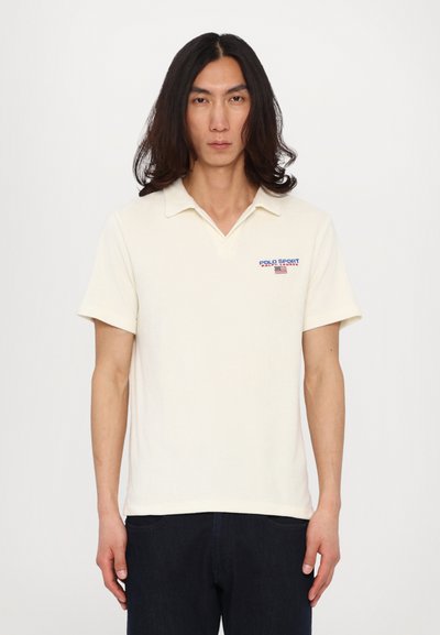 Polo shirt in crème kleur, korte mouwen, V-hals, met het "POLO SPORT" logo in blauw en rood op de linkerborst, gemaakt van zachte katoen.