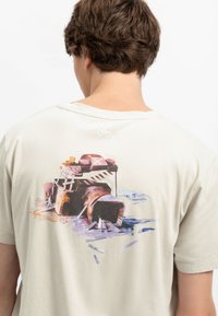 Lichtbeige t-shirt met een kleurrijke grafische print van een camera op de achterkant, van zacht katoen en met een ronde hals.