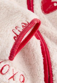 Obleka iz flisa z zadrgo v svetlo roza barvi z rdečimi poudarki in vezenim napisom. Ima mehak, teksturiran površino in poudarke v obliki srca.