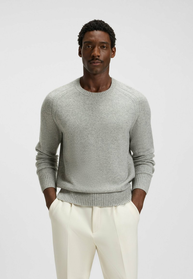Maglione grigio chiaro in morbido tessuto a maglia, con polsini e orlo a coste, maniche inserite, scollatura rotonda, abbinato a pantaloni crema.