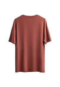 T-shirt à manches courtes couleur rouille en tissu doux. Présente un col rond et un petit logo brodé à l'arrière près du col.