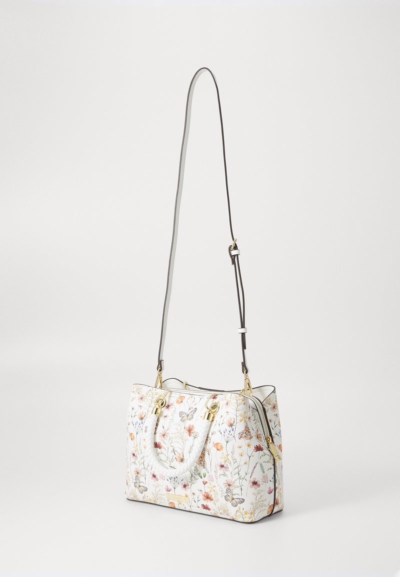 Sac à main à motif floral en blanc, avec des éléments en métal doré, des poignées supérieures doubles et une bandoulière réglable. Texture lisse et forme structurée.
