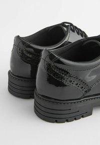 Schwarze Lacklederschuhe mit runder Zehe, detaillierten Perforationen, flachen Schnürsenkeln und einer dicken, geriffelten Sohle. Glatte, glänzende Textur.