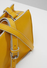 Borsa a mano in pelle gialla con rifiniture grigie, caratterizzata da un design strutturato, tracolla regolabile e chiusura con zip. Dettaglio della superficie testurizzata visibile.