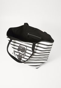 Geantă tote din pânză cu dungi orizontale alb-negru, având un design grafic. Interiorul are un căptușeală neagră și un buzunar cu fermoar.