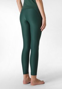 Leggings verdi realizzati in materiale elastico, caratterizzati da una texture liscia, un design aderente e cuciture a contrasto lungo i lati.