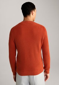 Maglione lavorato a maglia arancione con texture a costine, scollo rotondo e polsini aderenti, visto da dietro. L'orlo inferiore è leggermente curvato.