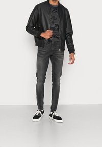 Černá kožená bomber bunda s žebrovanými manžetami, tričko s camo potiskem, šedé slim fit džíny a černé tenisky s bílými podr�ážkami.