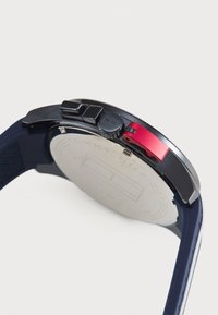 Orologio nero con cassa in acciaio inossidabile, pulsante di accento rosso, cinturino in gomma blu testurizzata e retro in argento liscio.
