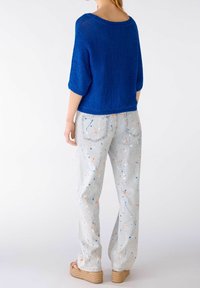 Niebieski sweter z dzianiny z szerokimi rękawami, zestawiony z jasnoszarymi dżinsami z kolorowymi plamkami. Całość dopełniają espadryle.