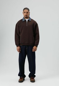 Bruine zip-up trui met denim kraag, gecombineerd met donkerblauwe losse jeans en bruine laarzen. Gladde stof en ontspannen pasvorm.