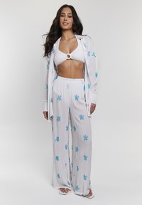 Witte, gestructureerde strandoutfit met blauwe sterrenzeevissen borduursels; bestaat uit een cropped top met een ringdetail en wijde broekspijpen.
