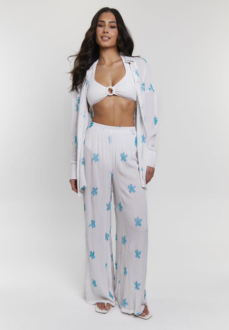Witte, gestructureerde strandoutfit met blauwe sterrenzeevissen borduursels; bestaat uit een cropped top met een ringdetail en wijde broekspijpen.