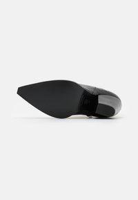 Chaussure noire en cuir à bout pointu avec une finition lisse et un design épuré. La semelle est plate avec une légère texture et un detailing minimal.