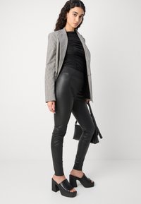 Houndstooth mustriga bleiser, must ruched top, must nahkleskede ja must platvormi mules. Lisavarustusena on väike käekott.