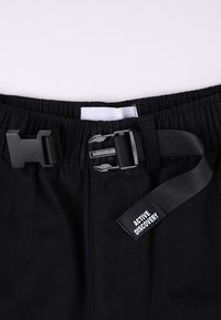 Schwarze Hose mit elastischem Bund, Kunststoffschnalle und verstellbarem Riemen. Verfügt über ein gewebtes Etikett mit der Aufschrift „ACTIVE DISCOVERY“.