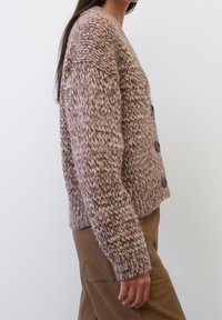 Prodlévaný kardigan v jemných růžových a krémových odstínech, s volnějším střihem, kulatým výstřihem a pěti tmavými knoflíky po celé délce přední části. Texturovaná látka.
