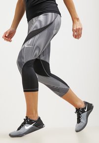 Leggings Nike en negro y gris con un diseño estampado, de longitud capri más corta y acentos texturizados. Llevados con zapatillas deportivas negras.