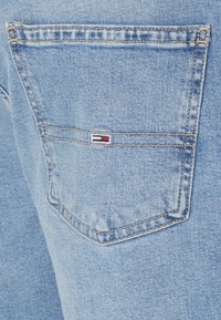 Světle modrá džínovina má zadní kapsu s malým vyšitým logem v červené, bílé a modré barvě. Šité detaily zvýrazňují okraje.