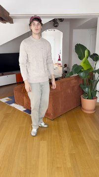 Άτομο με ανοιχτό μπεζ πουλόβερ και γκρι παντελόνι στέκεται δίπλα σε μια ριγωτή πορτοκαλί καναπέ. Ένα μεγάλο πράσινο φυτό βρίσκεται σε μια τερακότα γλάστρα δίπλα τους.