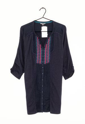 Blusa azul marino de manga larga con cierre de botones al frente, bordado colorido en rosa y azul en el pecho, y mangas abatibles colgada en una percha negra.