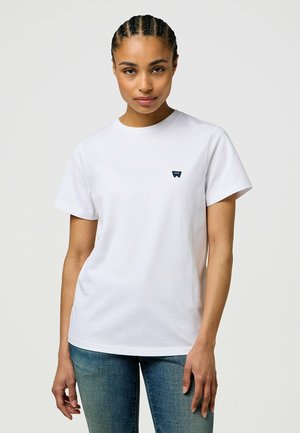 Witte katoenen t-shirt met korte mouwen, ronde hals en een klein marineblauw logo op de linkerkant van de borst. Gecombineerd met aangesloten spijkerbroek.
