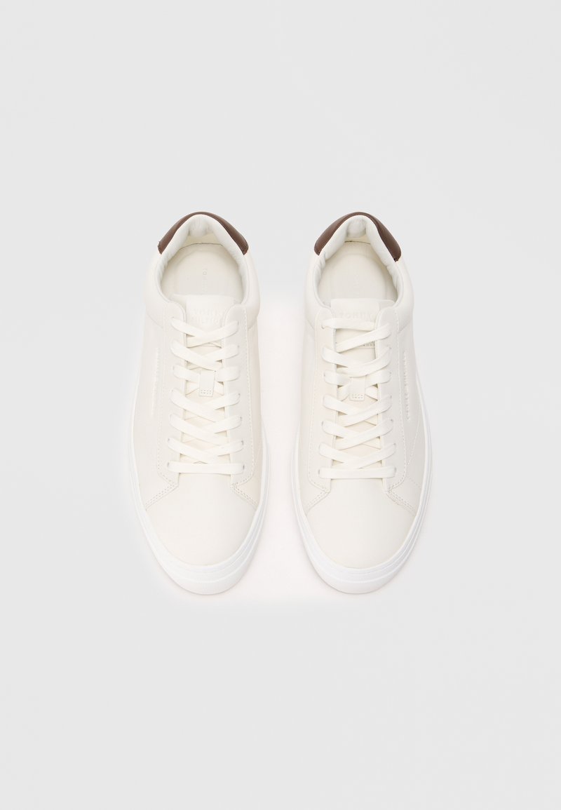 White leather sneakers with white laces, rounded toes, and a brown accent on the heel. Smooth texture and minimalistic design.