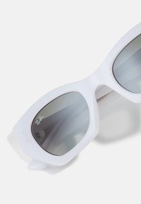 Ochelari de soare albi cu un design geometric, lentile gri și logo-ul Ray-Ban. Au un cadru gros din plastic și o formă unghiulară.