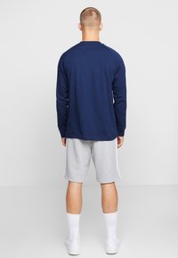 Camisa de manga larga azul marino con cuello redondo, combinada con pantalones cortos grises. La camisa presenta mangas raglán y una textura suave.