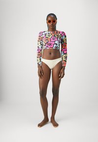 Haut de maillot de bain à manches longues avec un motif floral multicolore, associé à un bas de bikini couleur crème. Tissu lisse, design ajusté.