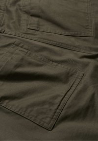 Olivgrön tyg med en slät textur som har en stor, platt ficka. Materialet verkar hållbart och mjukt, utformat för funktionalitet.