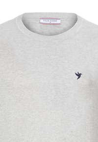 Un pull léger gris clair avec un petit logo d'oiseau sombre sur la poitrine gauche et une étiquette de marque Felix Hardy à l'intérieur du col.