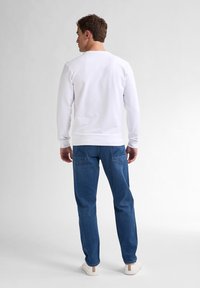 Camicia bianca a maniche lunghe abbinata a jeans blu, con tasche sul retro e una vestibilità comoda. Calzature casual completano l'outfit.