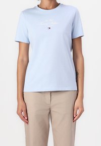 Ljusblå bomullströja med kort ärm, rund halsringning och logotext i vit och röd tryck. Enfärgad, avslappnad passform.