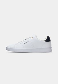 Fehér sneaker sima bőr felsőrésszel, arany fűzőlyukakkal, légáteresztő perforációkkal és tengerészkék sarok akcentussal. Rugalmas gumitalp.