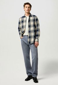 Miesten ruudullinen flanellipaita, joka on kermaan ja laivastonsiniseen, napitettu ja suoralla leikkauksella. Yhdistetty vaaleansinisiin suoralahkeisiin farkkuihin ja mustiin saappaisiin.