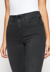 Svart högmidjade jeans med en slät denimtextur, utrustad med två framfickor och dubbelknäppning.