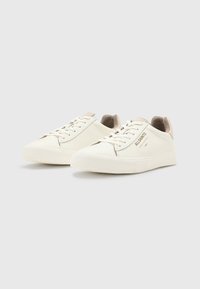 Weiße Ledersneaker mit strukturiertem Zehenbereich, beigen Wildlederelementen an der Ferse und flachen Schnürsenkeln. Verfügt über dezente Markenkennzeichnung an der Seite.