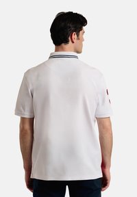 Camisa polo blanca de algodón, con mangas cortas, un cuello de canalé con rayas marinas y un pequeño logo rojo en una manga.