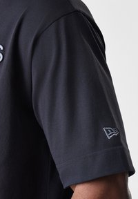 Černé tričko s krátkým rukávem a hladkým povrchem. Obsahuje jemnou výšivku loga na rukávu. Design s kulatým výstřihem.